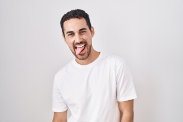 Obraz premium Handsome hispanic man standing over white background sticking tongue out happy with funny expression. emotion concept.