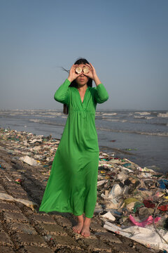 woman in green dress standing in plastic waste washed upon shore near ocean in Vietnam