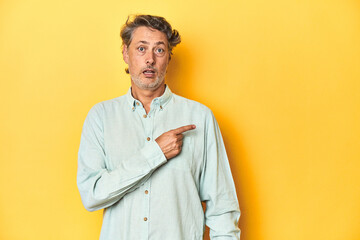 Middle-aged man posing on a yellow backdrop pointing to the side