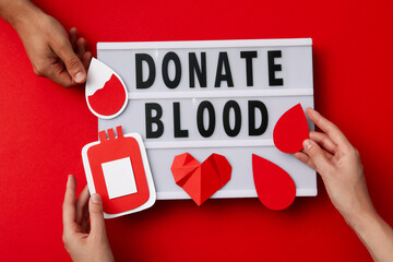 Paper container of blood in hand with red heart on red background. Blood donation