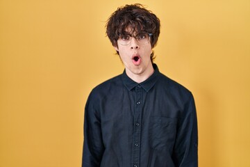 Obraz premium Young man wearing glasses over yellow background afraid and shocked with surprise expression, fear and excited face.