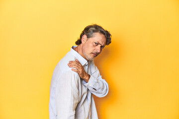 Fototapeta premium Middle-aged man posing on a yellow backdrop having a shoulder pain.
