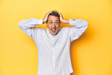 Middle-aged man posing on a yellow backdrop screaming, very excited, passionate, satisfied with something.