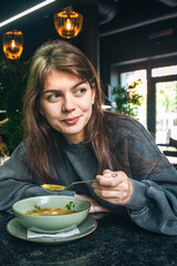 Attractive woman is eating vegetable soup in a cafe.