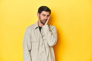 Caucasian man in grey shirt, studio shot on yellow who is bored, fatigued and need a relax day.