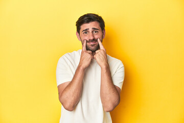 Caucasian man in white t-shirt on yellow studio background doubting between two options.