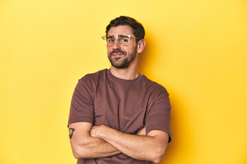 Man with arms crossed posing on a yellow studio background.