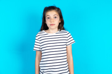 Stunned Caucasian kid girl wearing floral dress over blue background  stares reacts on shocking news. Astonished girl holds breath