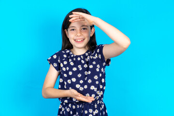 Caucasian kid girl wearing floral dress over blue background  gesturing with hands showing big and large size sign, measure symbol. Smiling looking at the camera.