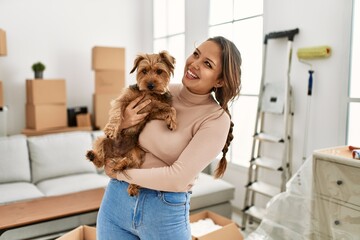 Young beautiful hispanic woman smiling confident hugging dog at new home