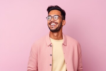 Fototapeta premium Portrait of young indian man in eyeglasses laughing against pink background