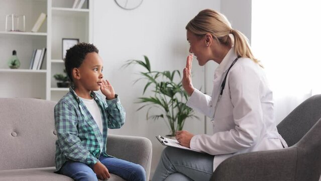 Happy female doctor giving high five to cute little African American boy patient at hospital consultation. A smiling pediatrician will cheer up a small child at the clinic. Healthcare concept.