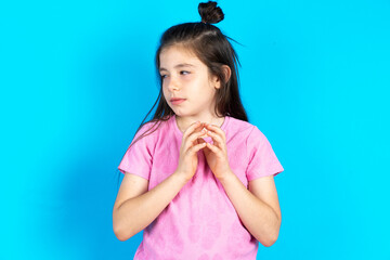 caucaisna kid girl wearing pink T-shirt over blue background steepled fingers and looks mysterious aside has great evil plan in mind