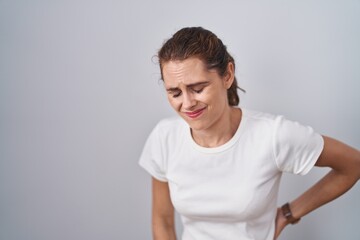 Beautiful brunette woman standing over isolated background suffering of backache, touching back with hand, muscular pain