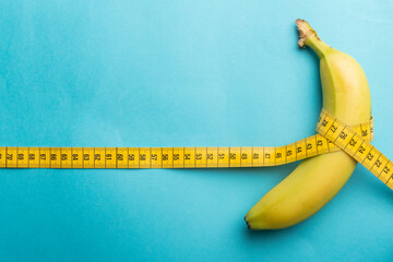 Size matter concept: a measuring tape around a banana on light blue background