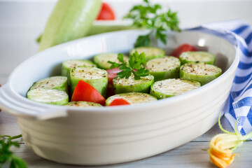 Raw zucchini with tomatoes prepared for baking in a ceramic form.