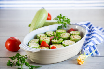 Raw zucchini with tomatoes prepared for baking in a ceramic form.