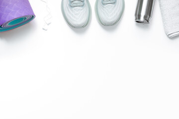 New light blue green female running shoes headphones metal water bottle towel and rolled yoga mat on emty white background. Stylish monochrome shoes for active people that incorporate new health