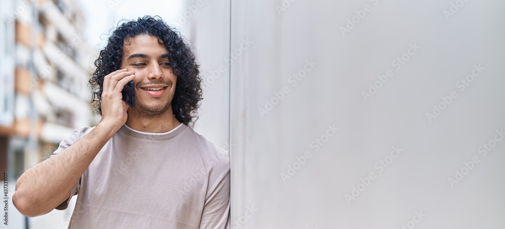 Sticker Young latin man smiling confident talking on the smartphone at street