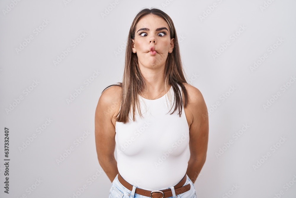 Sticker hispanic young woman standing over white background making fish face with lips, crazy and comical ge