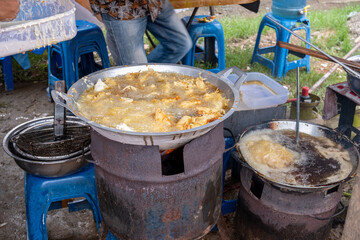 food vendors on the side of an Indonesian road are frying rissol or risoles in hot oil on a large frying pan