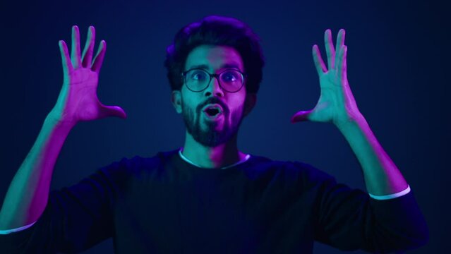 Close up man portrait Muslim coder in neon studio ultraviolet background Arabian man Indian guy make mind explosion gesture cyberspace hacking programming difficulties problem showing head boom idea