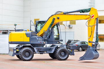 A wheeled construction excavator is parked in a paved car park on a bright day. - 637334478