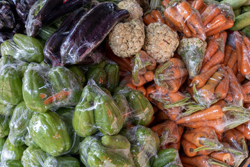 An assortment of fresh vegetables neatly packed in plastic, including vibrant bell peppers,...