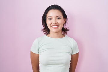 Hispanic young woman standing over pink background with a happy and cool smile on face. lucky person.