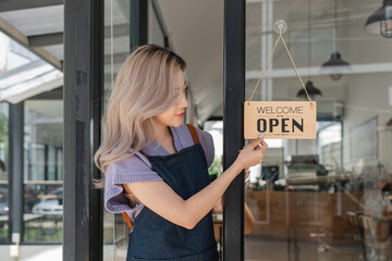 Portrait of a happy cafe owner standing at cafes entrance. Portrait of mature business in her coffee shop. Happy woman owner showing open sign in her small business shop