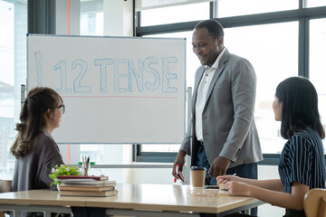 Positive friendly African American English tutor giving language courses to group of interested adults of different ages and nationalities sitting around table in classroom, Education concept