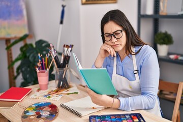 Young woman artist reading book drawing on notebook at art studio