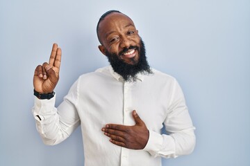 African american man standing over blue background smiling swearing with hand on chest and fingers...
