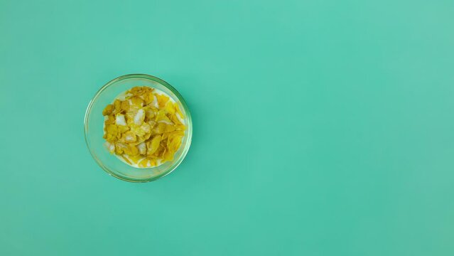 Stopmotion Time Lapse. Creating a Wholesome Breakfast with Corn Flakes in transparent Bowl on Green Background with copy space