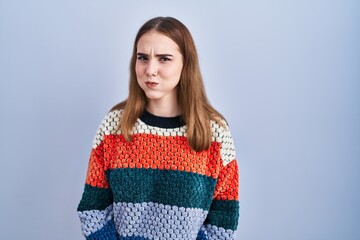 Young hispanic girl standing over blue background puffing cheeks with funny face. mouth inflated with air, crazy expression.