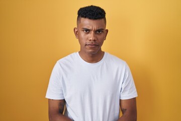 Young hispanic man standing over yellow background skeptic and nervous, disapproving expression on face with crossed arms. negative person.