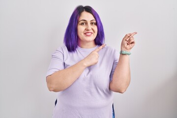 Obraz na płótnie Canvas Plus size woman wit purple hair standing over isolated background smiling and looking at the camera pointing with two hands and fingers to the side.