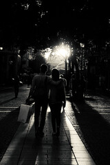 Couple (back view; unrecogniable people) after shopping walking at Parisian pedestrian street in golden sunset light. Back view. Paris, France. Black white historic photo - obrazy, fototapety, plakaty