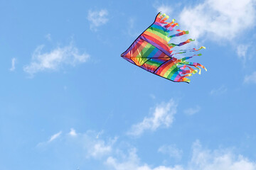 Kite in a blue sky. Rainbow Delta Kite flying among the clouds. Happy growing years moment. Outdoor time spending. Aspirations, target, inspiration concept. Freedom and summer holiday. Childhood dream