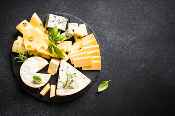 Cheese platter with craft cheese assortment on slate board at black background. Top view with copy...