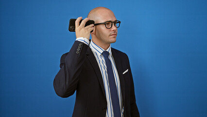 Young hispanic man business worker listening to voice message by smartphone over isolated blue background