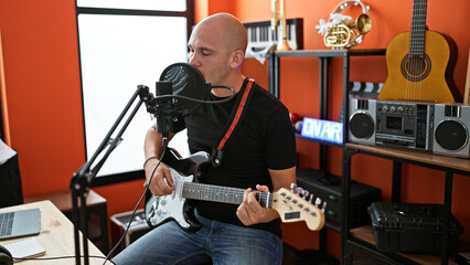 Young hispanic man musician singing song playing electrical guitar at music studio