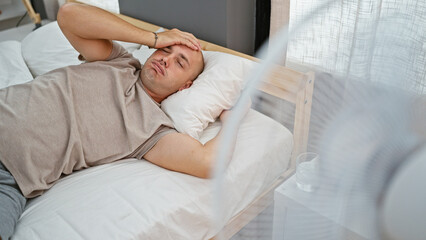 Young hispanic man lying on bed sweating using ventilator at bedroom