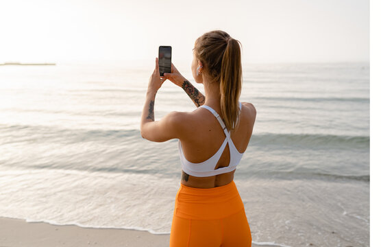 pretty young smiling woman doing sports in the morning in stylish sport outfit sportswear, using smartphone