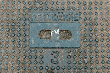Cast-iron manhole cover in the street with the inscription District heating and a number 3