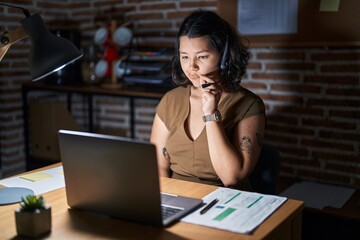 Young hispanic woman working at the office at night mouth and lips shut as zip with fingers. secret...