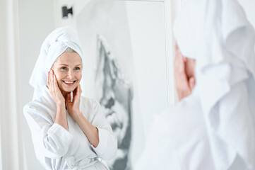 Focus on mirror reflection of smiling mid age woman touching face