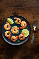 Shrimps with parsley and lime, overhead flat lay shot. Fried shrimp on a blue plate, shot from the top on a rustic wooden background