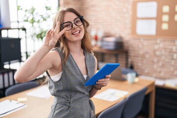 Caucasian woman working at the office wearing glasses doing peace symbol with fingers over face, smiling cheerful showing victory