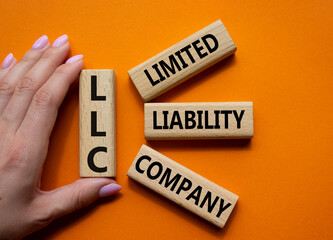 LLC - Limited liability company. Wooden cubes with word LLC. Businessman hand. Beautiful orange...